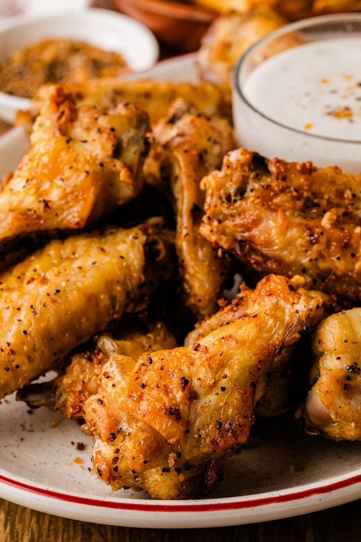 Close-up of crispy air fryer chicken wings with golden, seasoned skin on a plate with a red rim.