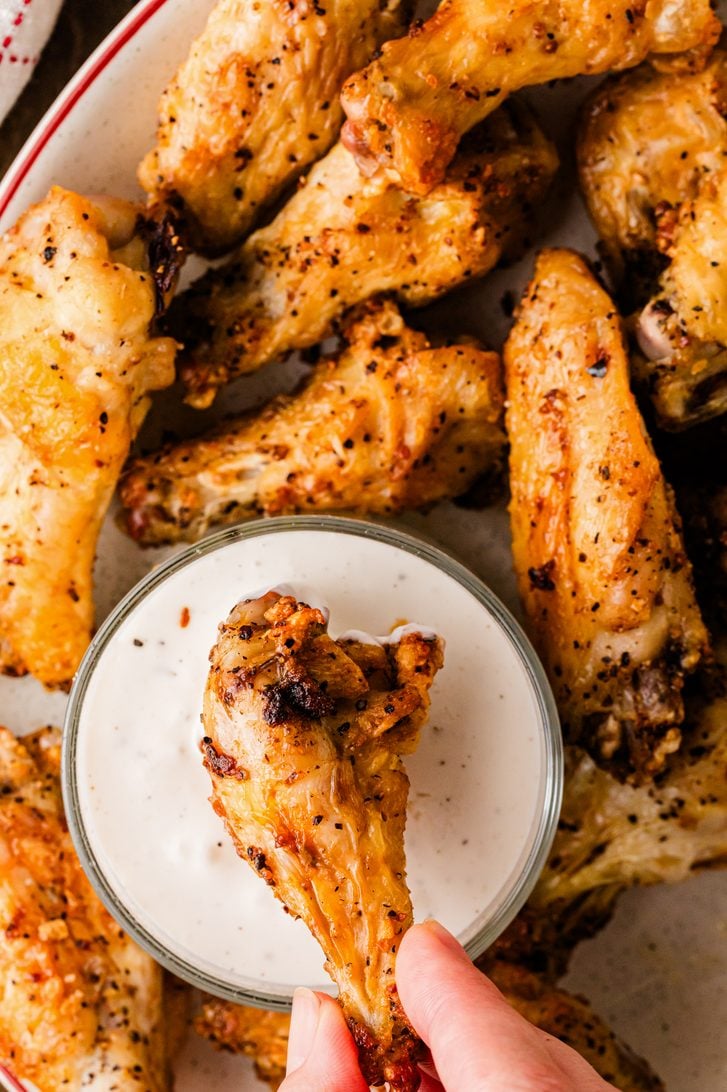 Hand dipping a crispy air fryer chicken wing into a bowl of ranch dressing.