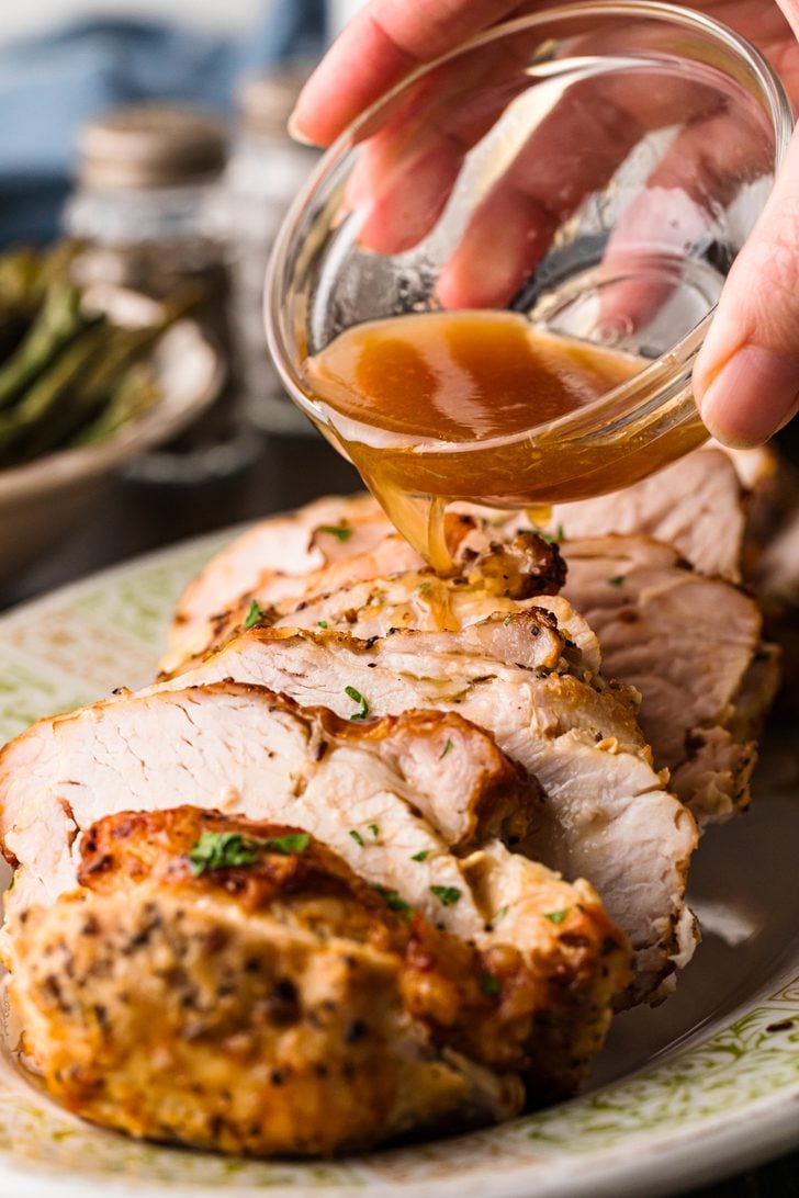 Air Fryer roasted turkey breast being drizzled with drippings ready to serve on a platter.
