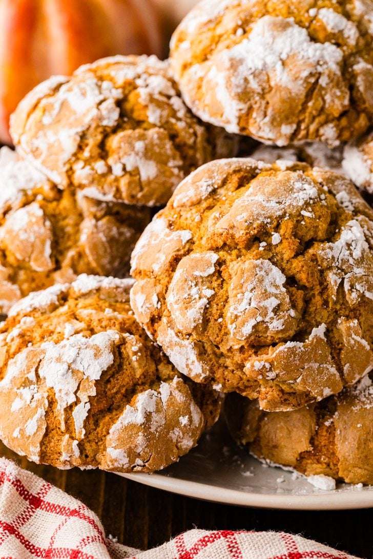 Plate piled high with soft pumpkin crinkle cookies coated in cracked powdered sugar.