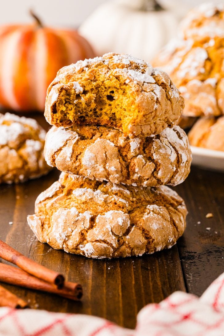 Stack of pumpkin crinkle cookies with a bite taken out of the top cookie, showing the soft, chewy center.