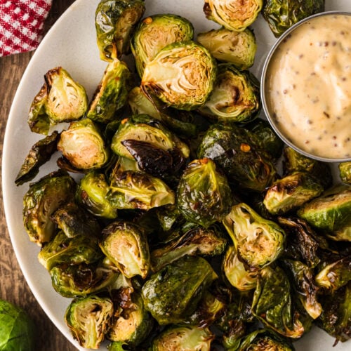 Crispy air fryer Brussels sprouts on a white plate with a small bowl of creamy dipping sauce.