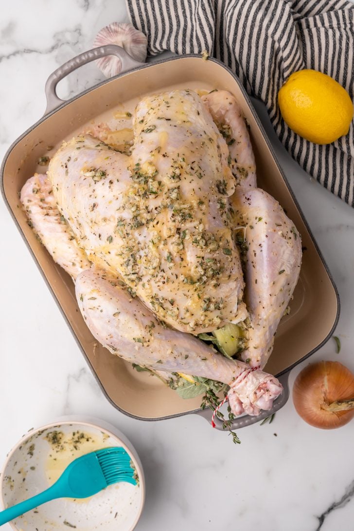 Whole uncooked turkey in a roasting pan prepped with butter and seasoning.